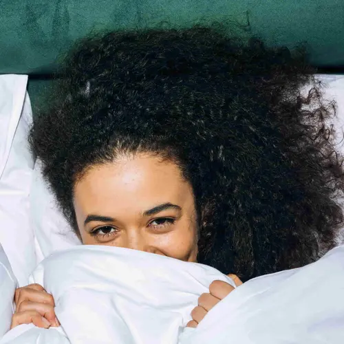 Woman lying in bed covering face with bedsheets